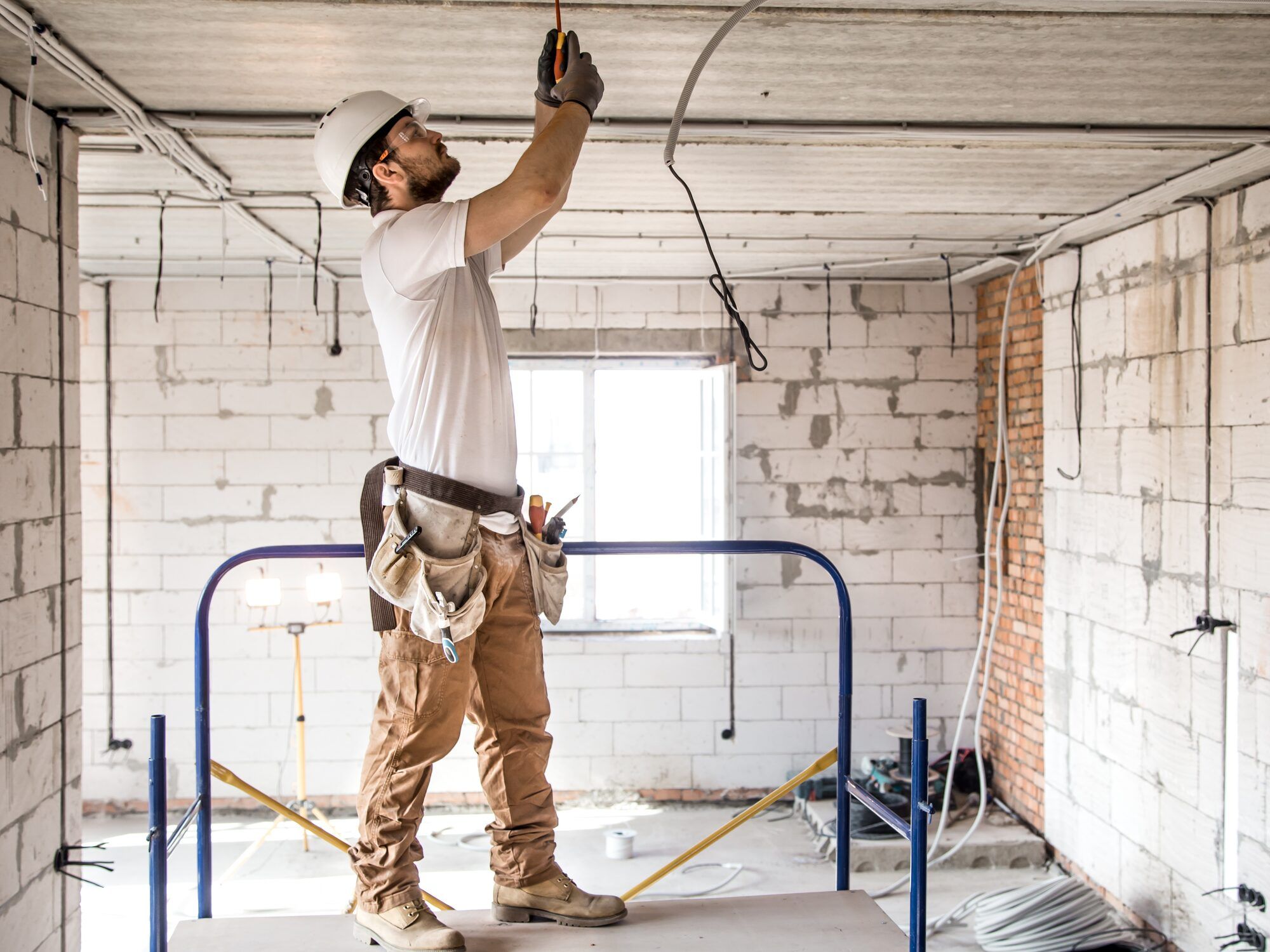 Electrician in a hard hat on a work platform fixing cables to a ceiling in a building under renovation